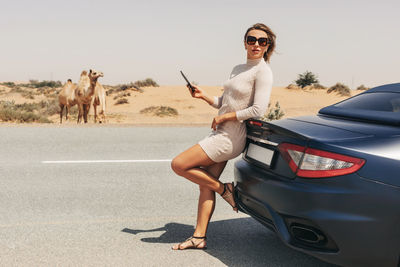 Portrait of an attractive girl with a phone in her hand by the car against the background 