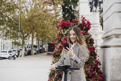 Young woman holding smart phone while standing on wall