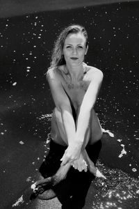 High angle view of naked woman sitting on wet sand at beach