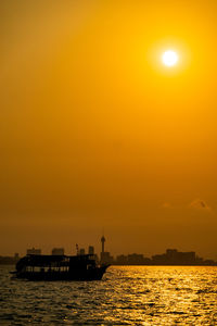 Silhouette ship in sea against orange sky