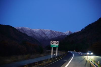 Road leading towards mountains against clear blue sky