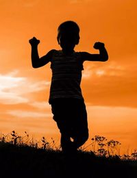 Silhouette man standing on field against orange sky