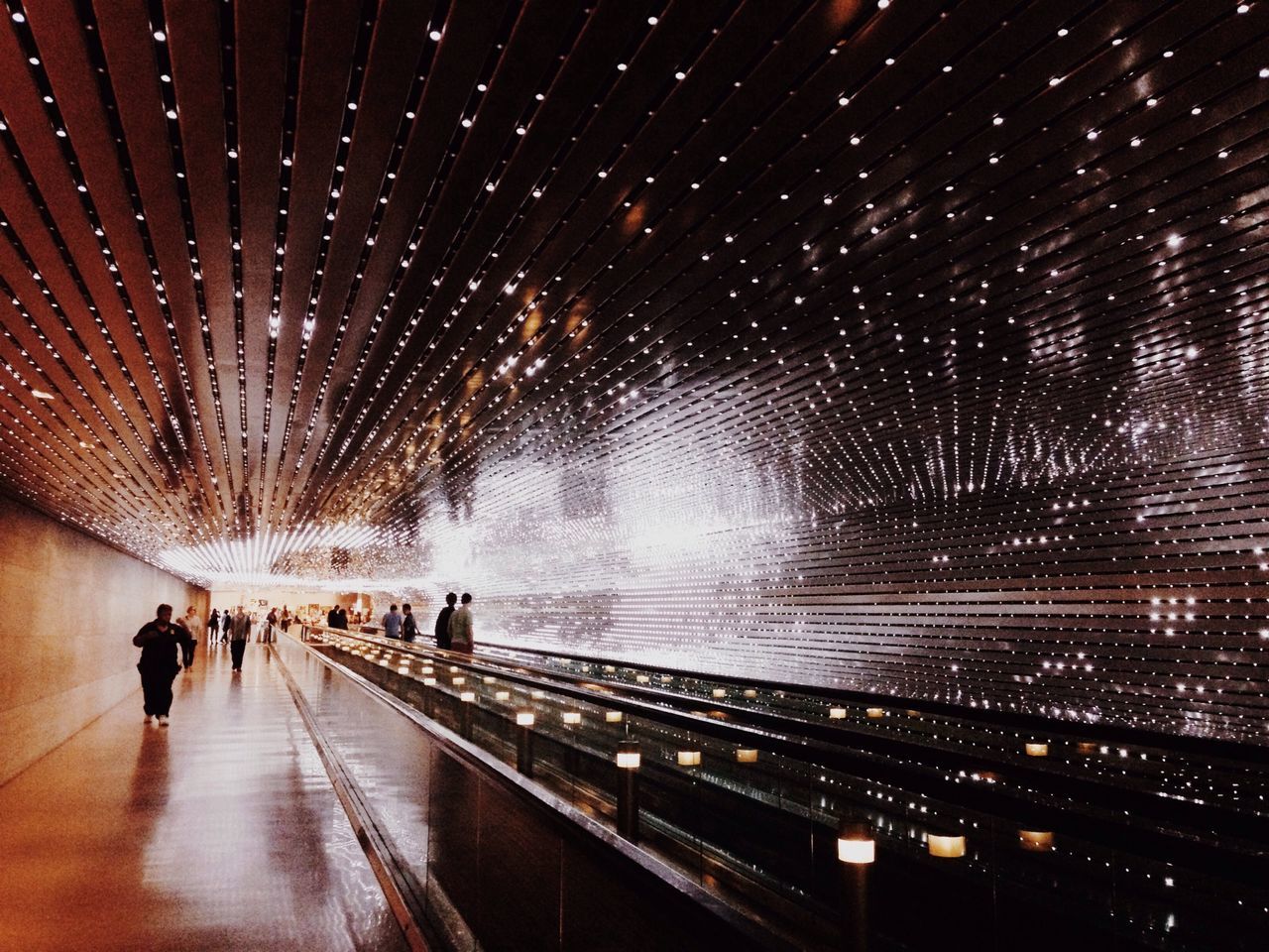 illuminated, night, men, lifestyles, motion, leisure activity, walking, indoors, person, large group of people, tunnel, lighting equipment, full length, long exposure, blurred motion, the way forward, medium group of people, travel, group of people