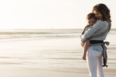 Mother carrying son while standing at beach