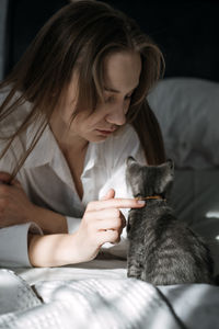 Candid portrait of young woman is resting with kitten pet on the bed at home one sunny day.