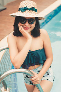 Portrait of smiling woman wearing sunglasses and hat in swimming pool