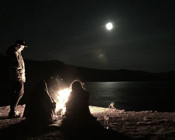 Silhouette people standing by lake against sky at night