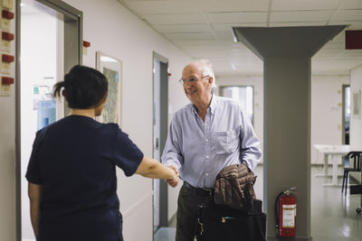 Smiling senior man greeting female medical staff standing at hospital