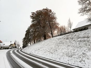 Snow covered road by trees against clear sky