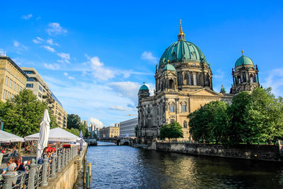 View of buildings by river in city against sky