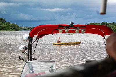 People in boat sailing on river against sky