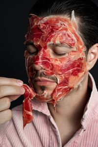 Close-up of young man with facial mask against black background