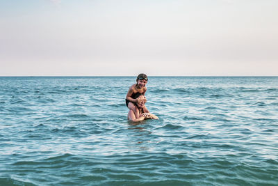 Full length of shirtless man in sea against sky