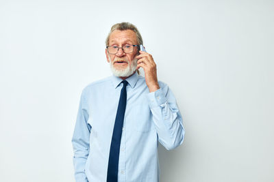Portrait of senior man talking on phone against white background