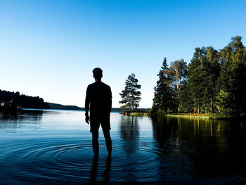 Rear view of silhouette man standing by lake against sky