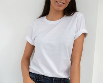 Portrait of a smiling young woman standing against white wall