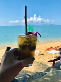 Midsection of man holding drink at beach against sky