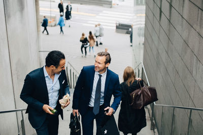 High angle view of smiling mature male business colleagues moving up on staircase in city