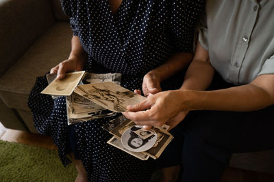 Midsection of woman holding old photos while sitting on floor