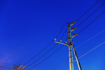 Low angle view of electricity pylon against blue sky