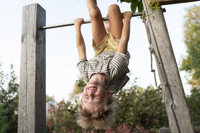 Cheerful boy hanging upside down on horizontal bar