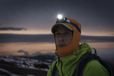 Close-up of man with illuminated headlamp against sky at dusk