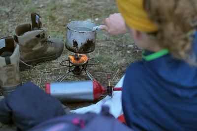 Female hiker making drink while leaning on bed at field during camping