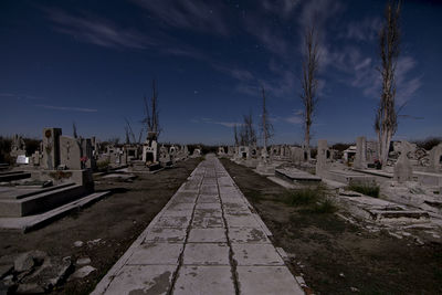 Footpath amidst gravestones in cemetery against sky at night
