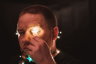 Close-up of man holding illuminated lighting equipment in darkroom