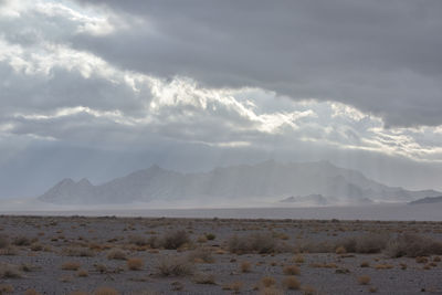 Scenic view of desert against sky view of mountain slightly covered by clouds with sun light raise