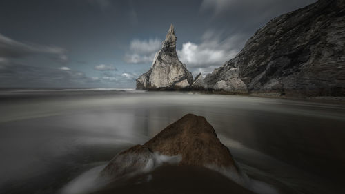 Scenic view of sea by mountain against sky