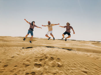 People jumping on beach against clear sky