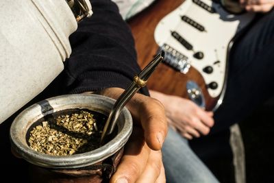 Cropped hand of man holding yerba mate with guitar on sofa