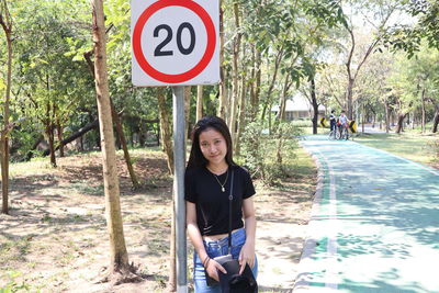 Portrait of woman leaning against information sign by road