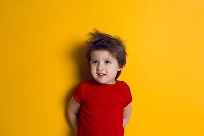 Cheerful baby boy in red t-shirt stands on yellow background