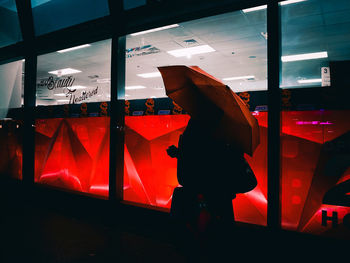 Silhouette person standing by illuminated window at night