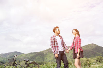 Young couple with bicycle on mountain against sky