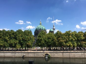 Church and fernsehturm by river in city against sky