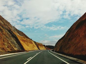 Empty road amidst rock formations against sky