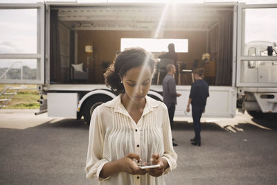 Businesswoman using smart phone with colleagues and portable office truck in background