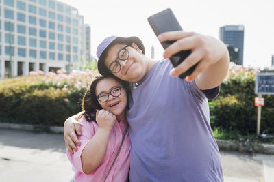 Smiling brother taking selfie with sister through mobile phone on sunny day