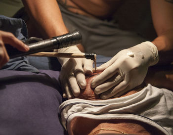 Cropped hands of people making tattoo on man shoulder with tools