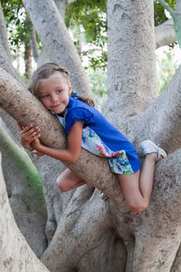 Full length of girl sitting on tree trunk outdoors