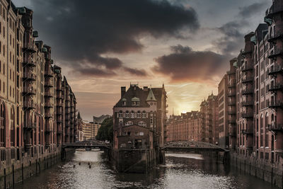 Canal amidst buildings against sky during sunset