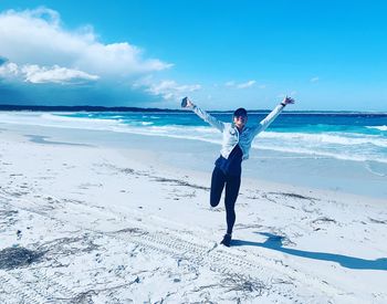 Woman with arms raised standing at beach against sky