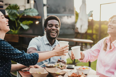 Smiling friends using mobile phone while sitting on table