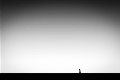 Silhouette person walking on land against clear sky