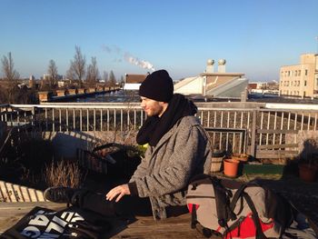 Side view of man sitting on railing against sky