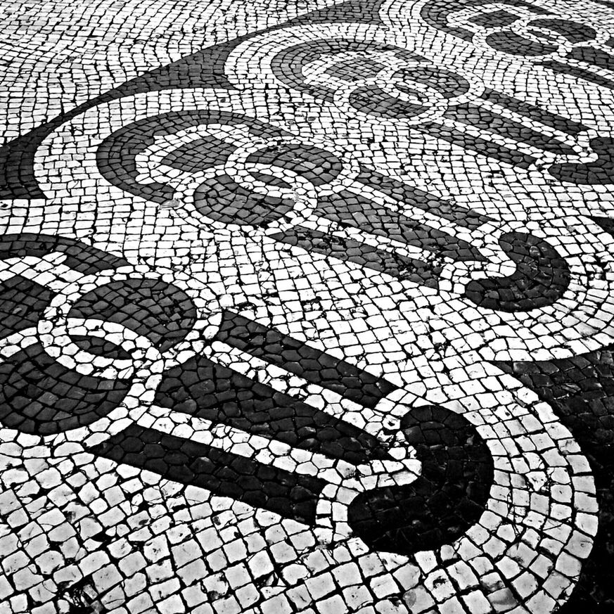 high angle view, cobblestone, street, paving stone, communication, text, pattern, sidewalk, footpath, pavement, western script, outdoors, creativity, manhole, art and craft, day, road marking, art, road, human representation