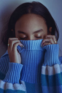 Close-up of eyes closed young woman covering face with sweater against wall